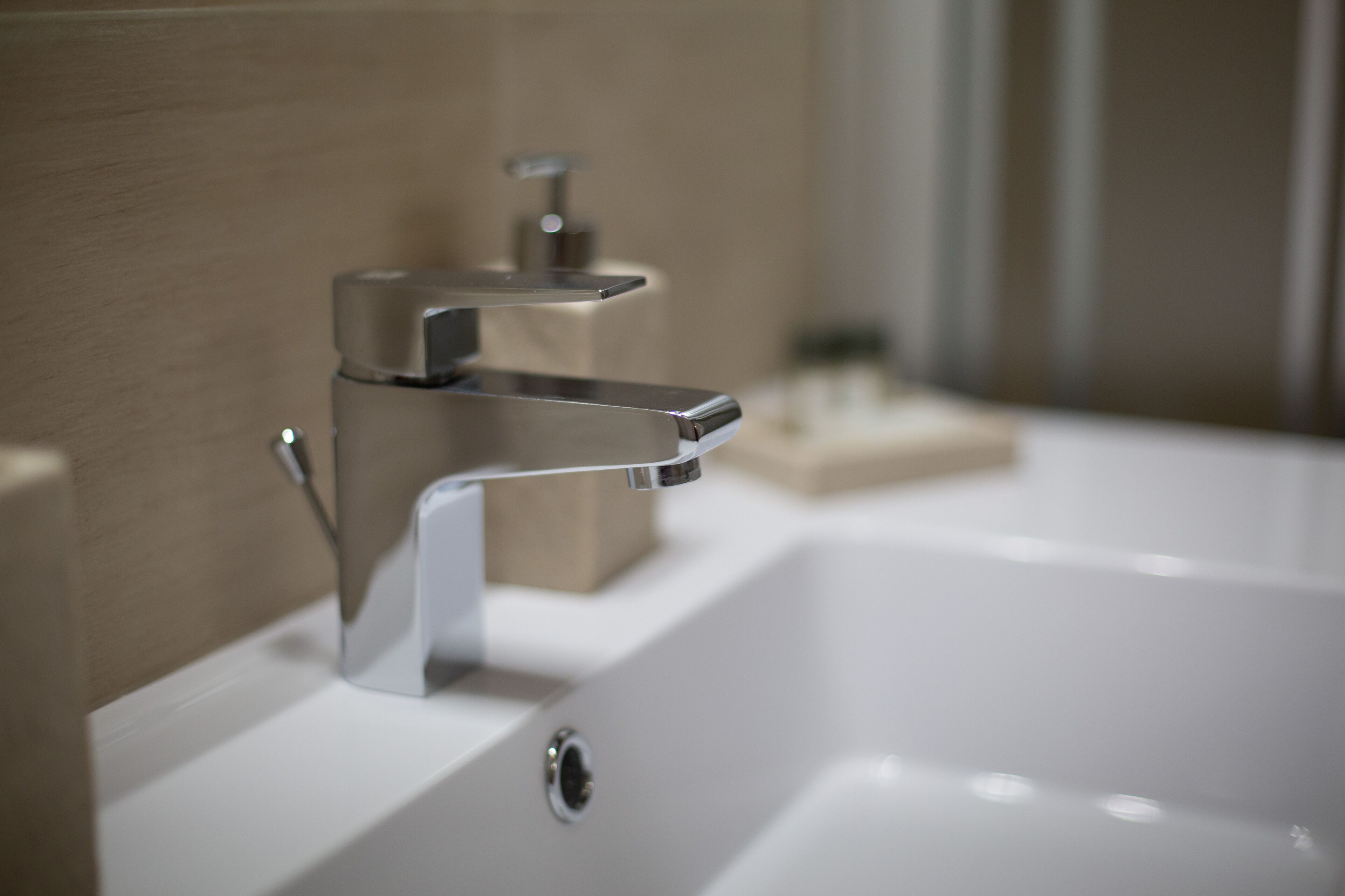 A modern bathroom with a chrome faucet, a white sink, and a beige soap dish.