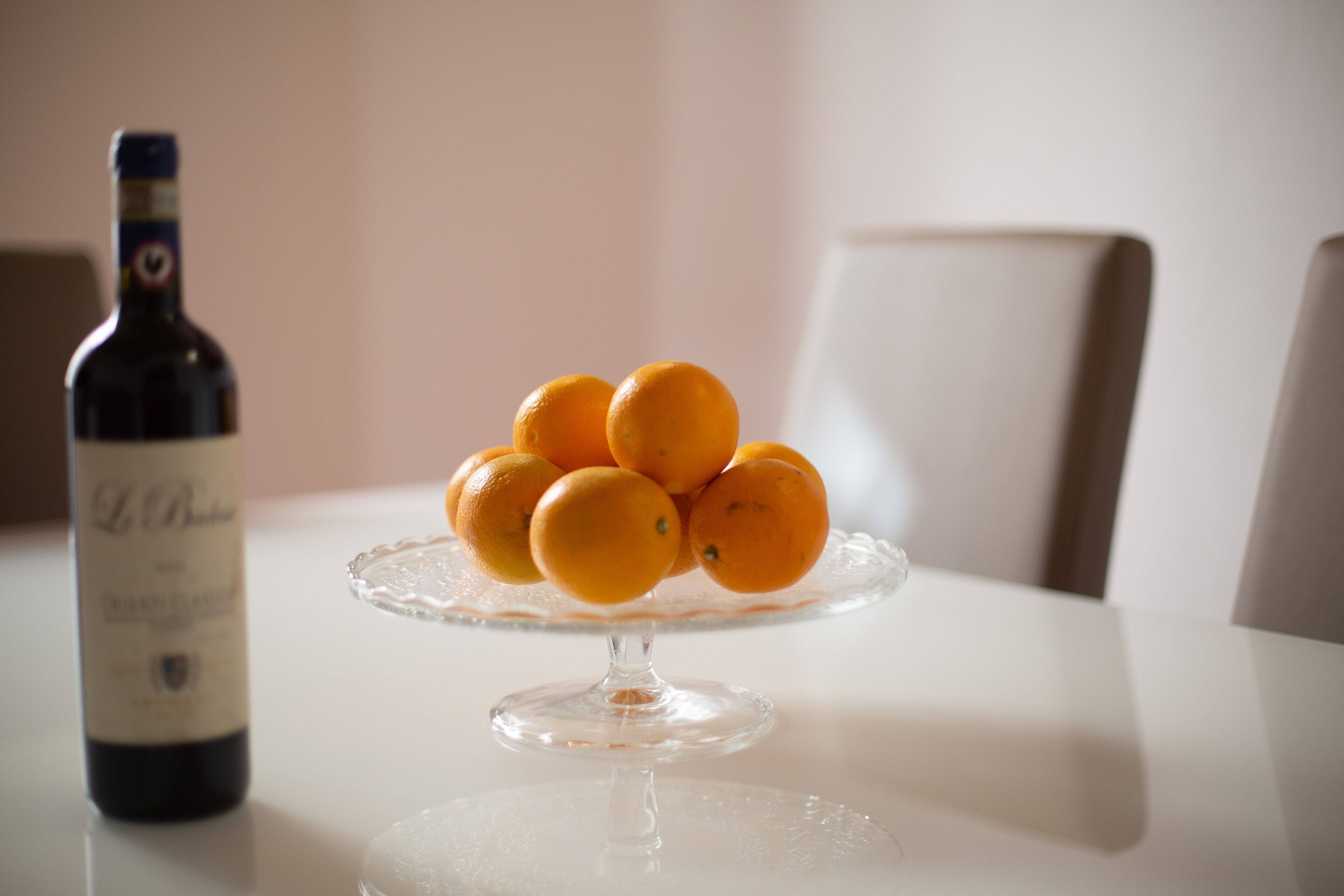 A table with a clear glass wine bottle and a glass plate with oranges.