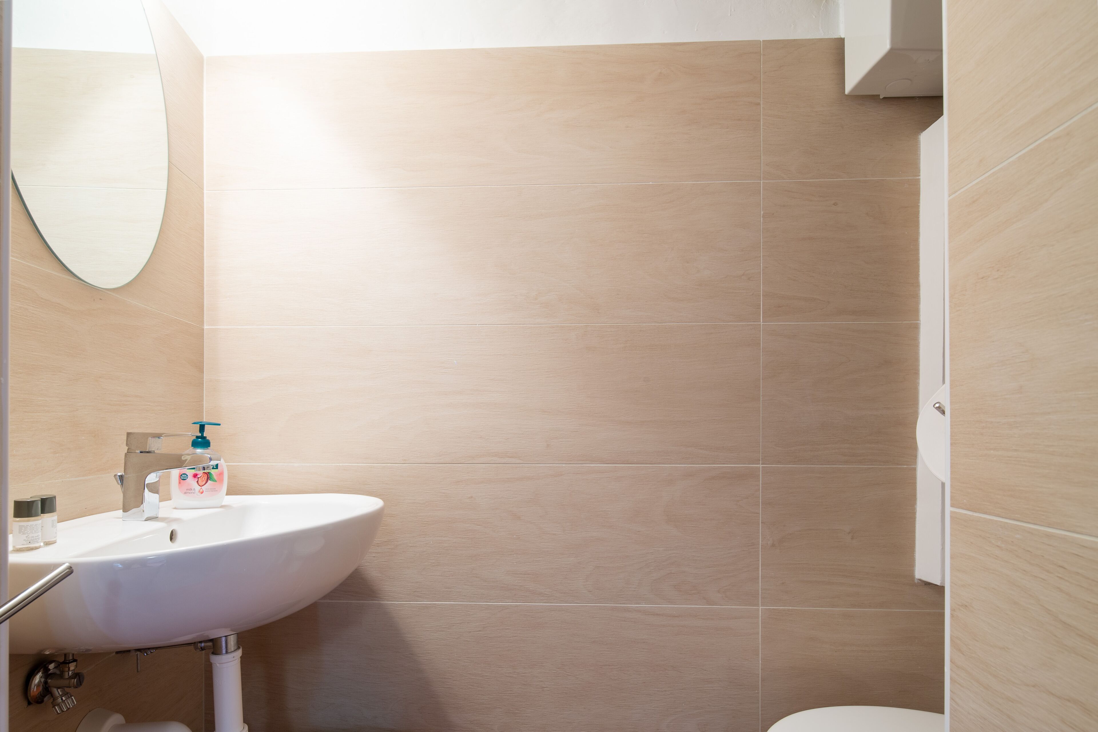 Ein Badezimmer mit weißem Waschbecken, einem Spiegel und beigen Fliesen.