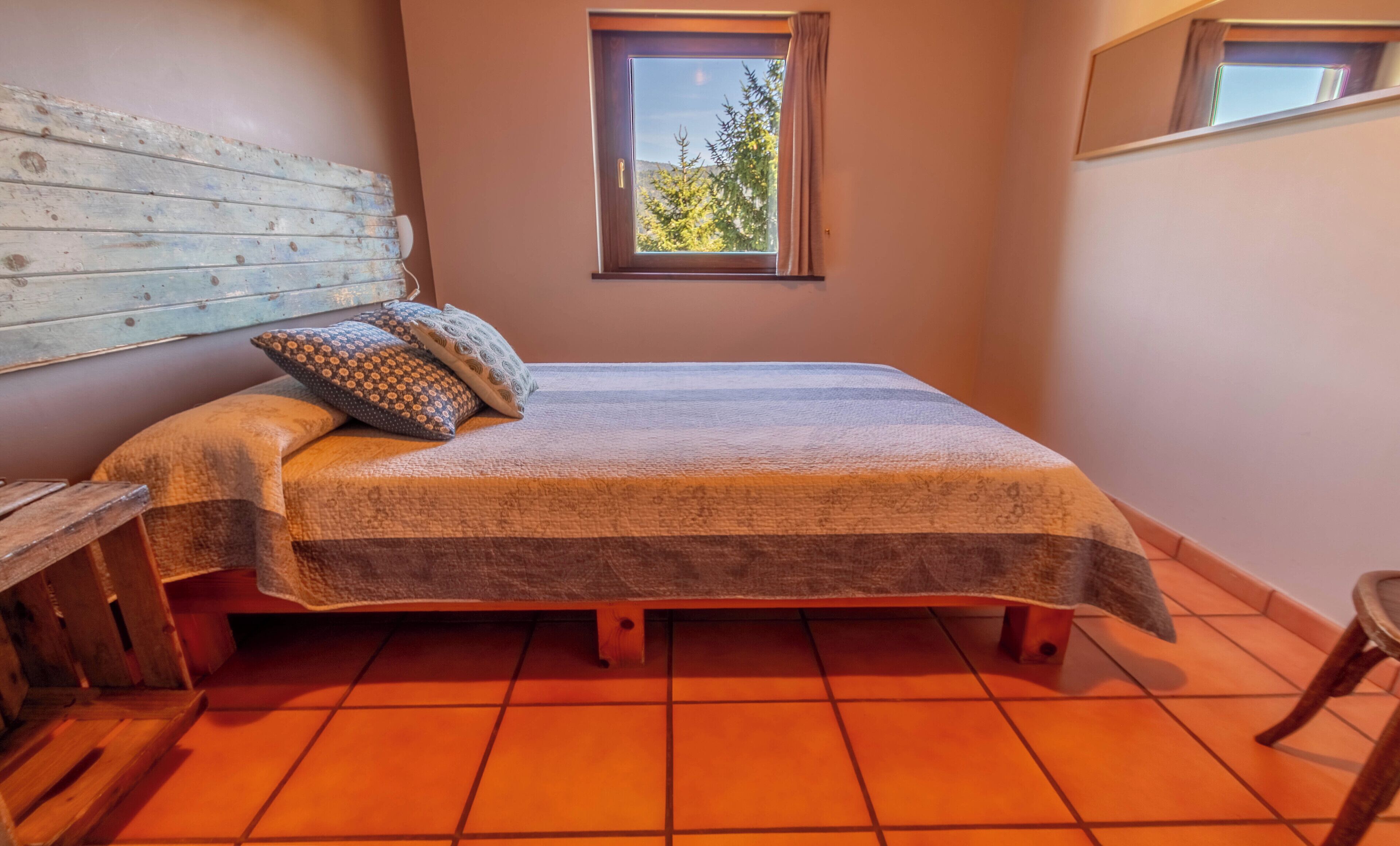 Un dormitorio con cama, almohadas, cabecera de madera, ventana y suelo de baldosas.