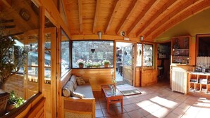 A cozy wooden cabin interior with a sofa, a table, and a view of the outdoors through large windows.