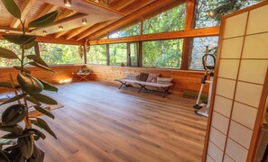 A spacious room with wooden floors, a bench, and large windows offering a view of trees. - Hostal Xalet Refugi Pere Carné - Hostel (Alp)