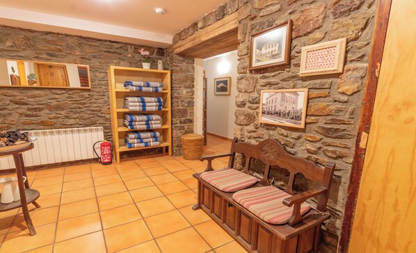 A cozy room with a stone wall, a wooden bench with cushions, a shelf with folded blankets, and a fire extinguisher. - Hostal Xalet Refugi Pere Carné - Hostel (Alp)