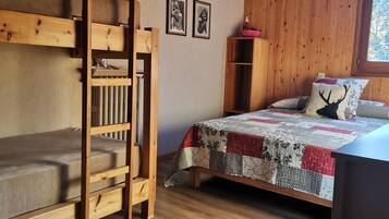 Un dormitorio con una cama litera, una colcha acolchada, un almohadón con diseño de ciervo y una estantería de madera con un tazón rosa.