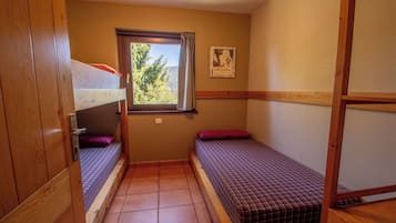 A small, compact room with two single beds, a window with a view of trees, and a poster on the wall.