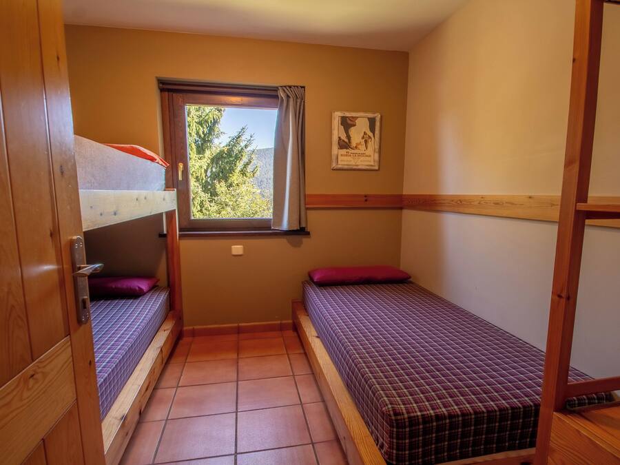 A small, compact room with two single beds, a window with a view of trees, and a poster on the wall.