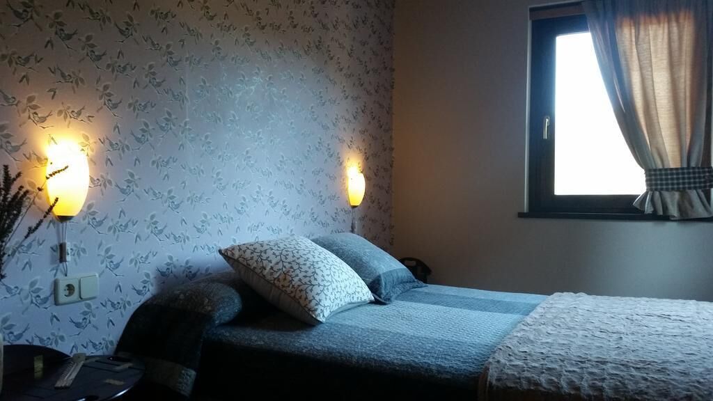 Un dormitorio con cama, dos lámparas de pared, un ventanal con cortinas y un papel tapiz estampado con motivos florales.