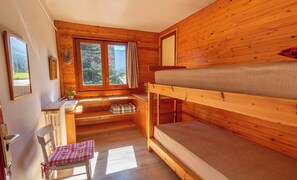 A compact wooden cabin room with bunk beds, a small desk, a chair, and a window with a view of trees. - Hostal Xalet Refugi Pere Carné - Hostel (Alp)