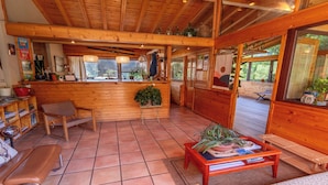 A wooden interior with a reception desk, seating area, and large windows.