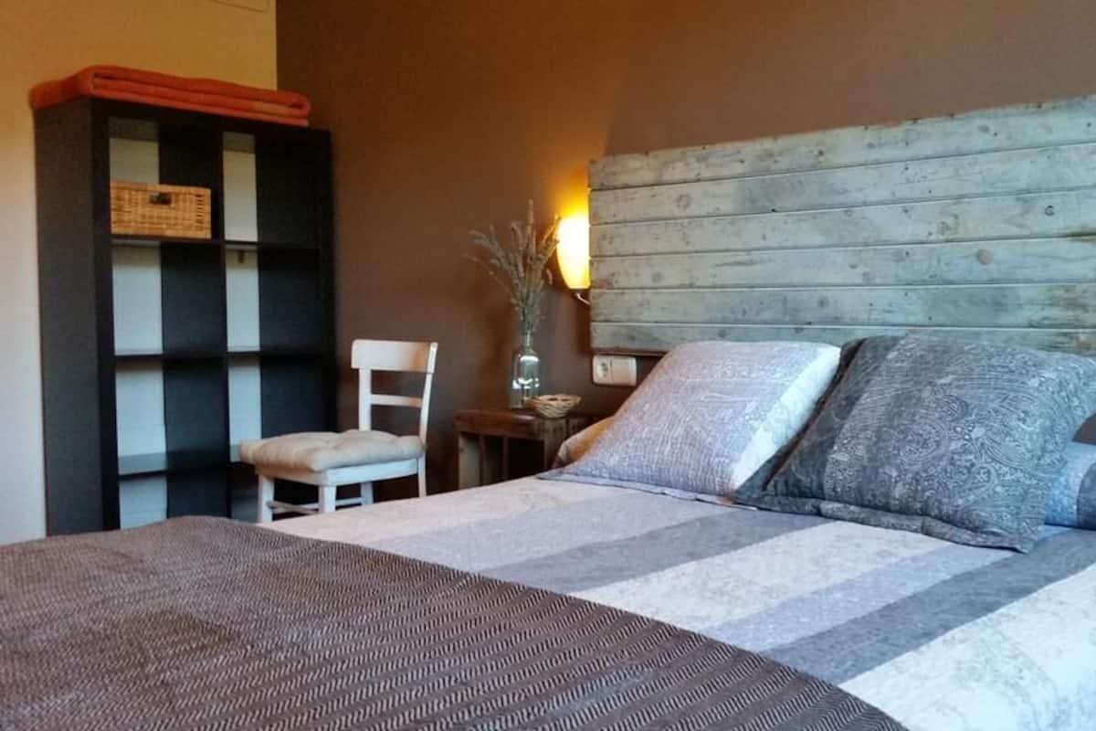 Ein Schlafzimmer mit einem Bett, einem Sessel, einem Nachttisch und einem Holzkopfteil.