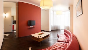 A modern living room with a red wall, a flat-screen TV mounted above a wooden coffee table, and a red leather sofa. - Apart Kiev Zlatoustovskaya 50-1 (Kyiv)