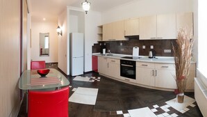 A modern kitchen with a refrigerator, oven, and sink. There is a dining area with a glass table and red chairs. The floor has a geometric tile pattern. - Apart Kiev Zlatoustovskaya 50-1 (Kyiv)