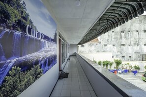 Un pasillo con un mural de cascada, suelo de baldosas y una zona cubierta con mesas y sillas.