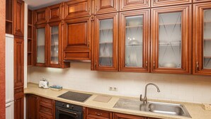 A kitchen with wooden cabinets, a stainless steel sink, a built-in oven, and a red patterned rug. - Apart Kiev Zlatoustovskaya 50-2 (Kyiv)