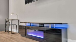 A modern entertainment center with a built-in fireplace, a flat-screen TV mounted above, and a chair to the left. - Bright 3BR Mid-City home with private patio & fenced yard. Steps to streetcar, near FQ & Superdome (New Orleans)