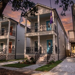 A two-story building with a balcony, a front door with a wreath, and a flag. - Bright 3BR Mid-City home with private patio & fenced yard. Steps to streetcar, near FQ & Superdome (New Orleans)