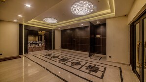 Un hall d’entrée spacieux, doté d’un sol en marbre poli, d’un magnifique lustre et d’une salle de conférence visible au fond.