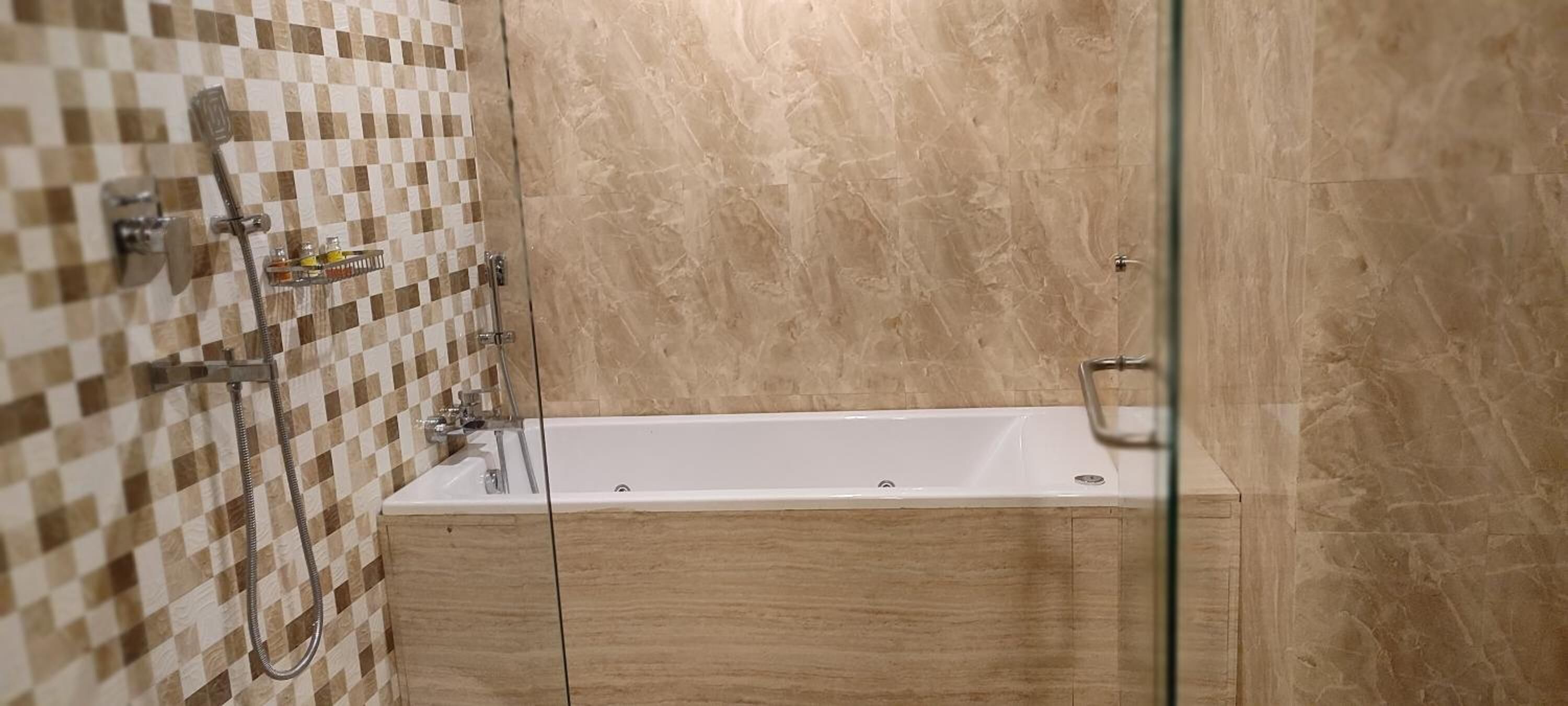 Un baño con pared de azulejos a cuadros, una bañera y un box de ducha de cristal.