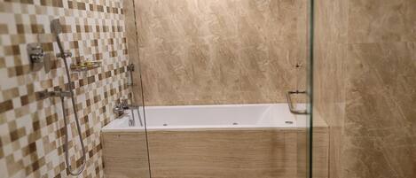 Un baño con pared de azulejos a cuadros, una bañera y un box de ducha de cristal.