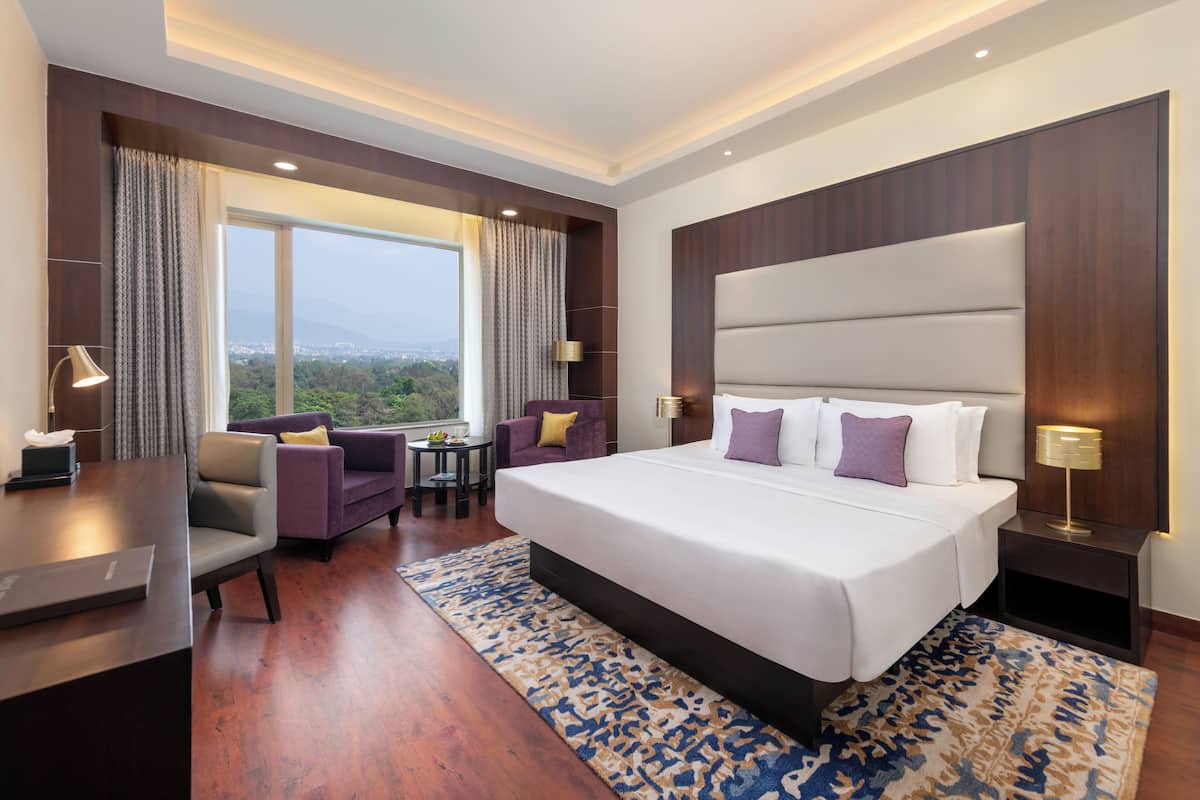 Habitación de hotel moderna con una cama grande, un escritorio, una silla y vistas a la ciudad.