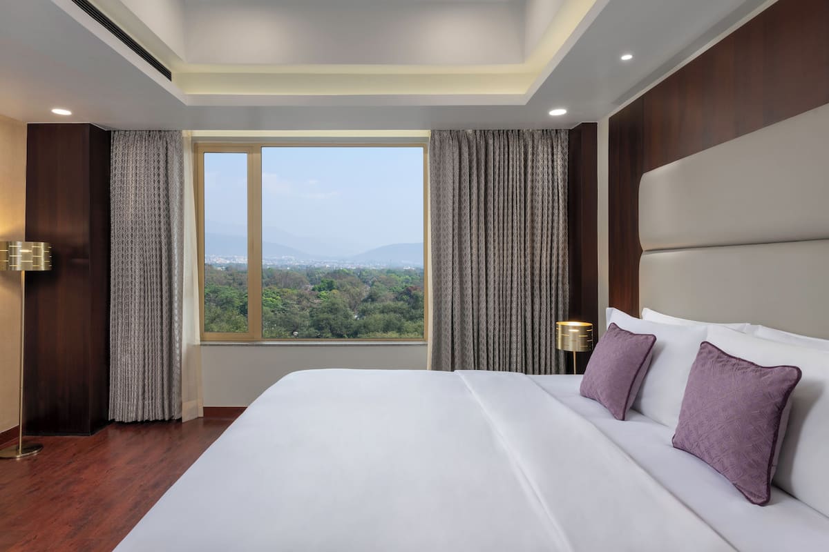 Habitación de hotel con una cama grande, vista a la ciudad y montañas, y un diseño moderno.