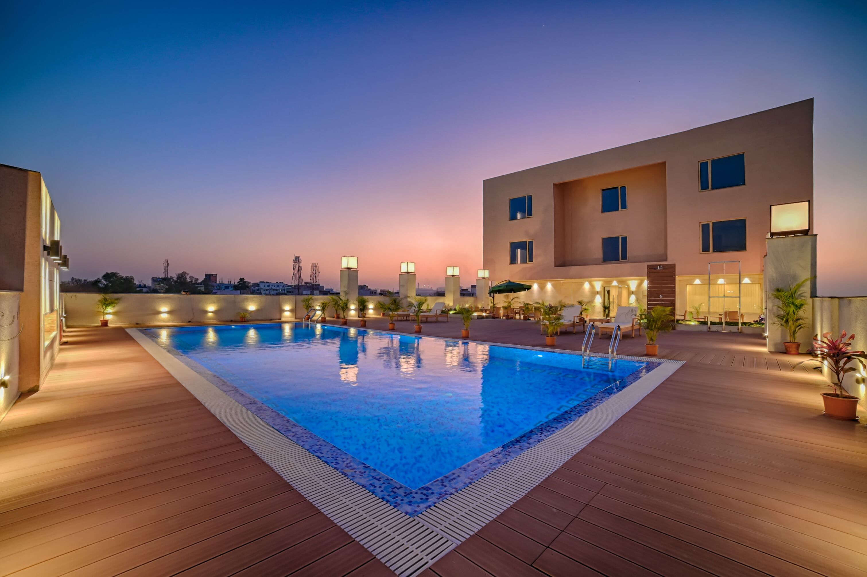 Piscina no terraço com deck de madeira, rodeada por edifícios modernos com janelas iluminadas.