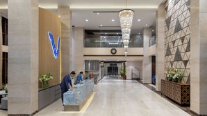 Un hall d’hôtel avec un comptoir d’accueil, un grand lustre et une horloge murale.
