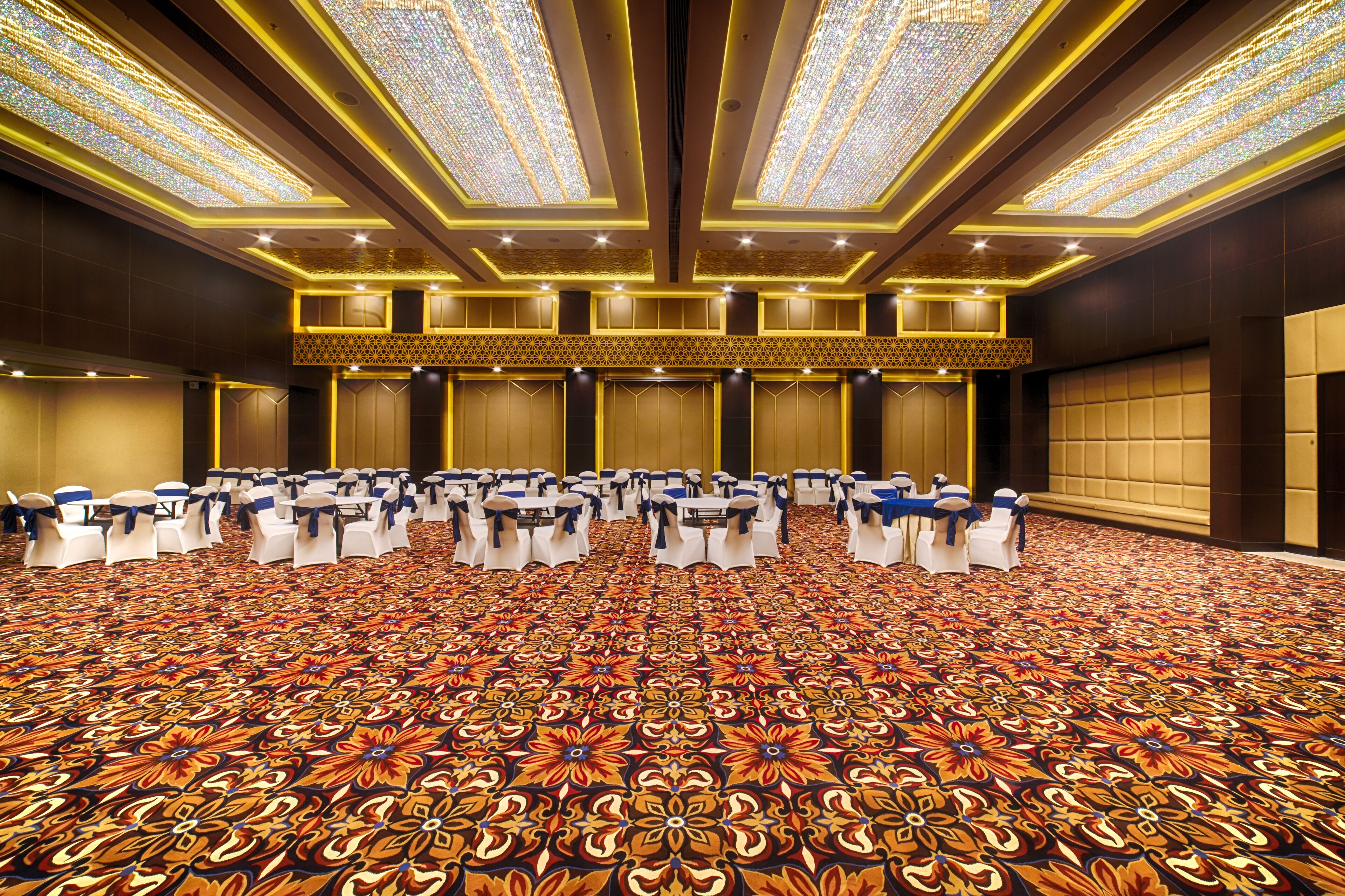 A large conference room with rows of tables and chairs, a patterned carpet, and a high ceiling with decorative lighting.