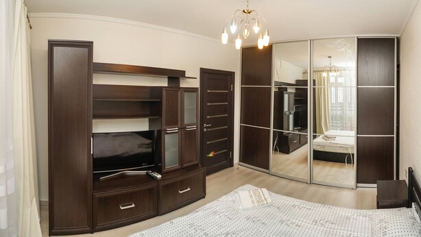 Quarto com guarda-roupa espaçoso, cama, espelho e lustre.
