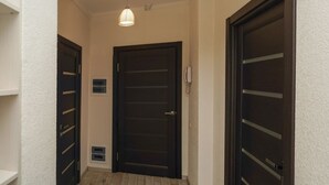 Um corredor com uma porta de madeira escura, um ponto de luz e uma pequena placa na parede.
