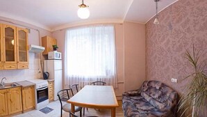 Ett kompakt bostadsutrymme med ett litet kök, en matplats och en sittgrupp med en soffa och en krukväxt.
