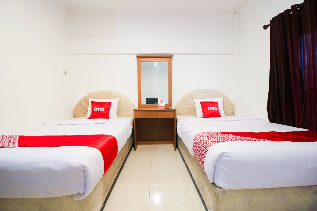 A hotel room with two single beds, a wooden nightstand, a mirror, and a red curtain.