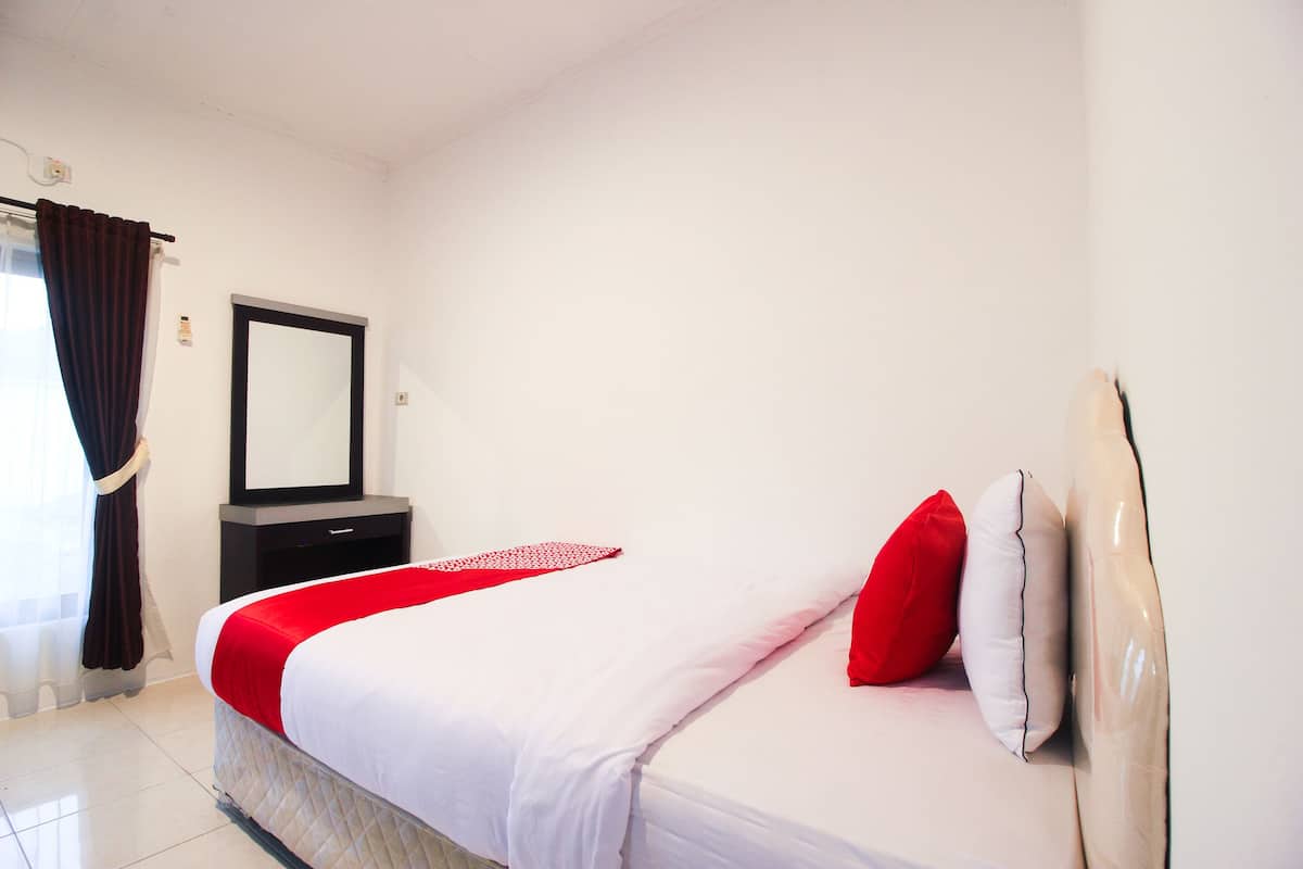 A neatly made bed with a red and white bedspread, a mirror above it, and a dark-colored nightstand beside it.