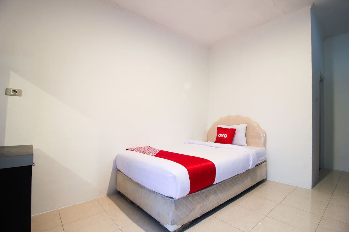 A single bed with a headboard, white bedding, and a red accent.