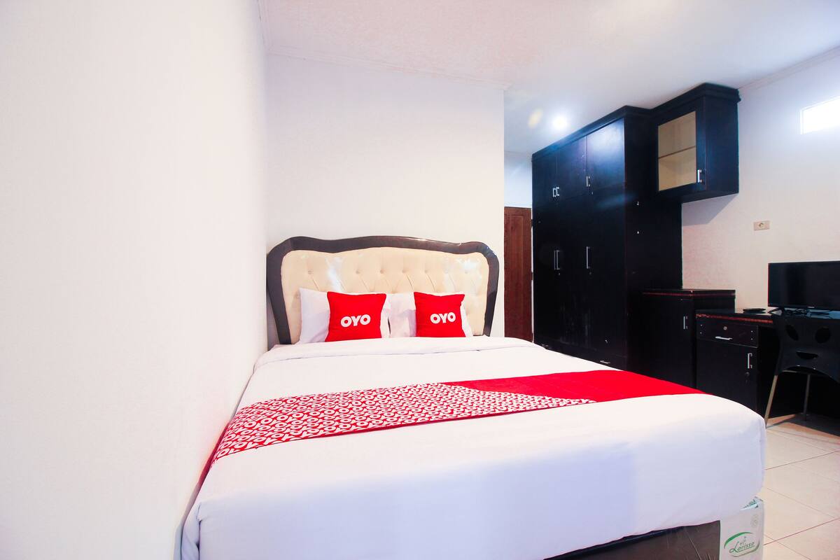 A neatly made bed with a red and white bedspread, two red pillows, and a headboard.