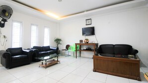 A living room with two black leather sofas, a wooden coffee table, a green plastic chair, a wooden side table, and a television on the wall. - OYO 1905 Davonsa  Homestay Syariah (Pekanbaru)