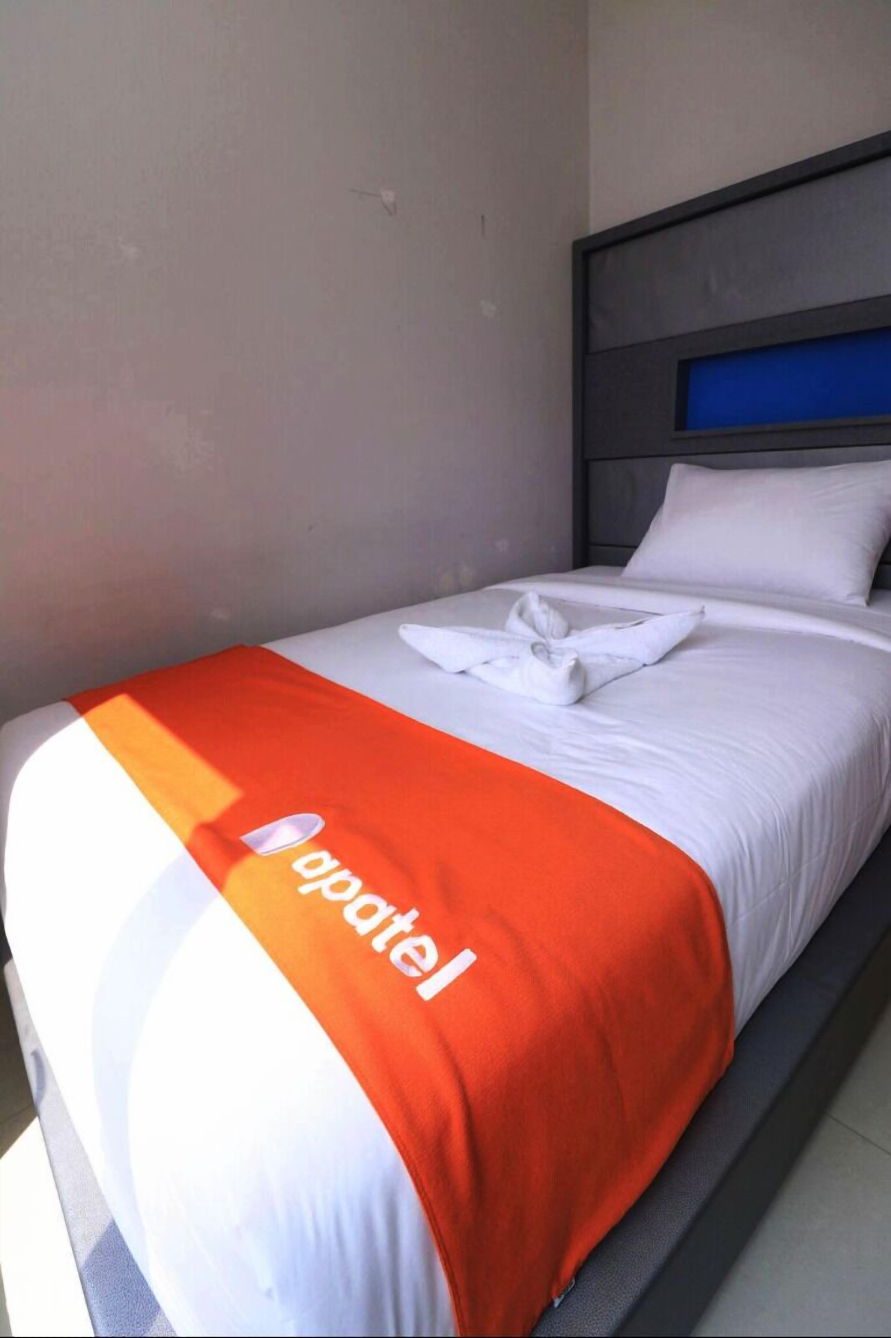 Una camera d'albergo con un letto, biancheria bianca e una coperta rossa con la scritta 'gpatel'.