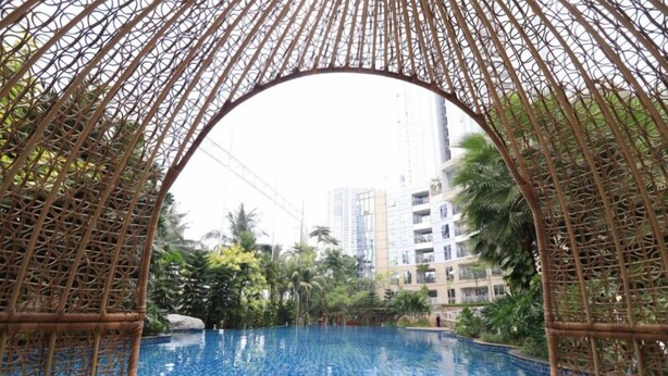 An indoor swimming pool with a bamboo archway, surrounded by greenery and high-rise buildings in the background. - Apatel The Mansion Tower Capilano (Jakarta)