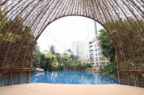 An indoor swimming pool with a bamboo archway, surrounded by greenery and high-rise buildings in the background. - Apatel The Mansion Tower Capilano (Jakarta)