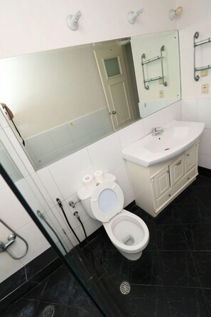 A bathroom with a white toilet, a white sink, and a mirror above the sink. - Apatel Apartement Kedoya Elok (Jakarta)