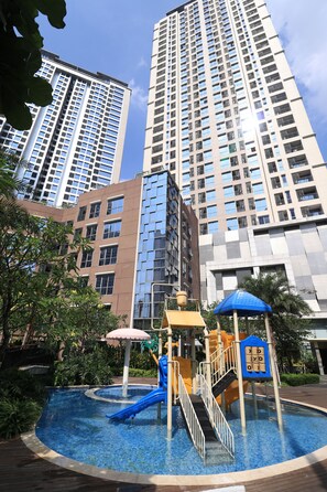 A children's play area with a slide and climbing structure, surrounded by tall buildings. - Apatel The Mansion Bougenville - Emerald (Jakarta)