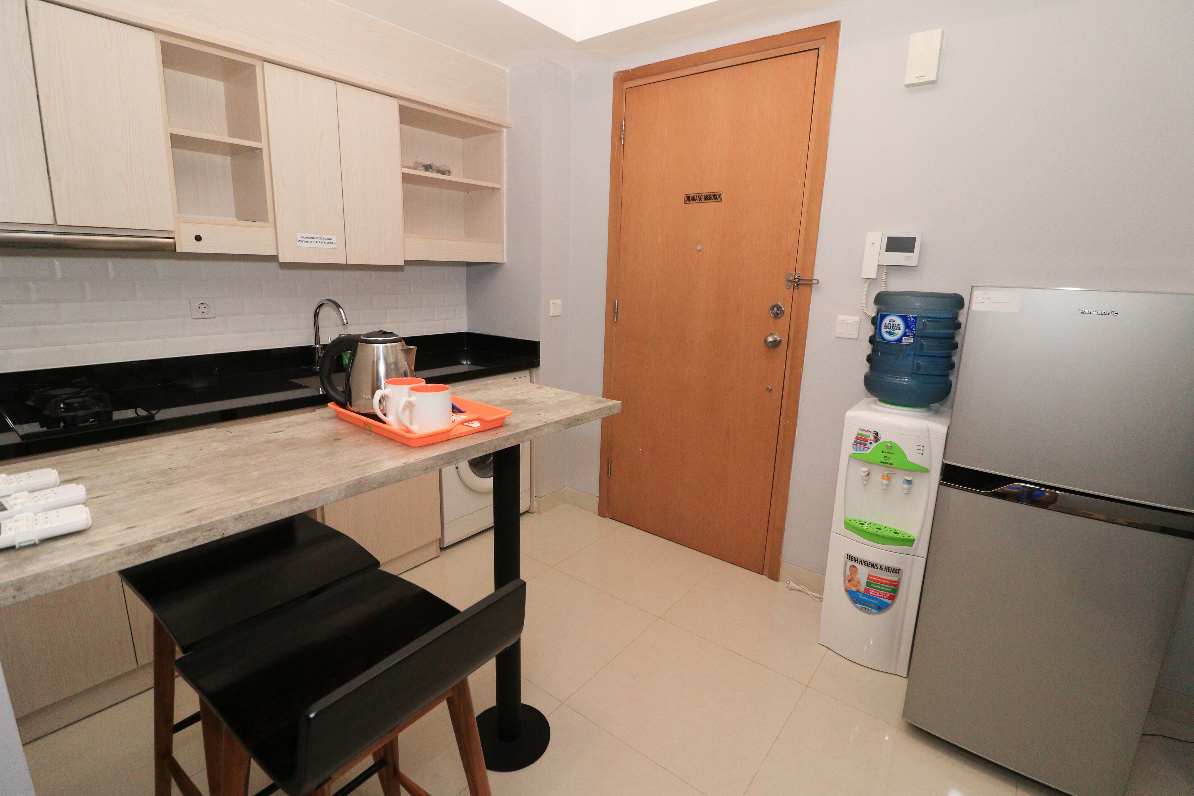 Una cocina compacta con encimera, lavabo, hervidor, refrigerador y dispensador de agua.