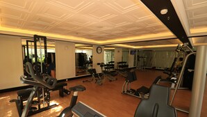 Un gimnasio con diversos equipos de ejercicio, un reloj en la pared y un espejo que refleja la sala.