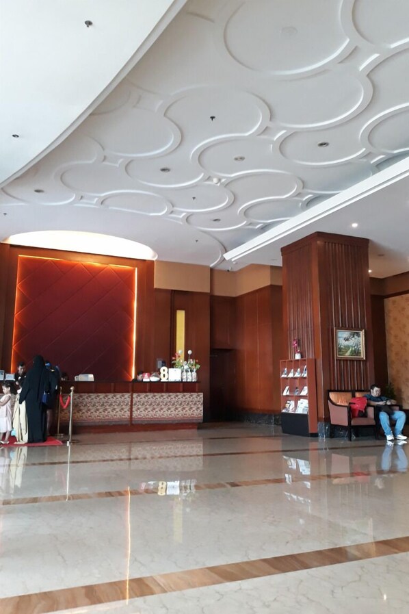 A hotel lobby with a reception desk, a large red accent wall, and a modern ceiling design.