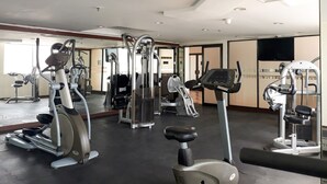 A gym with various exercise machines, a large mirror, and a television on the wall.