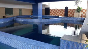 A swimming pool with blue mosaic tiles, a checkered wall, and a door in the background.