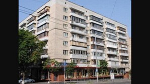 Ein mehrstöckiges Gebäude mit einheitlicher Fassade, Balkonen auf jeder Etage und einem Geschäftsbereich im Erdgeschoss mit Beschilderung.