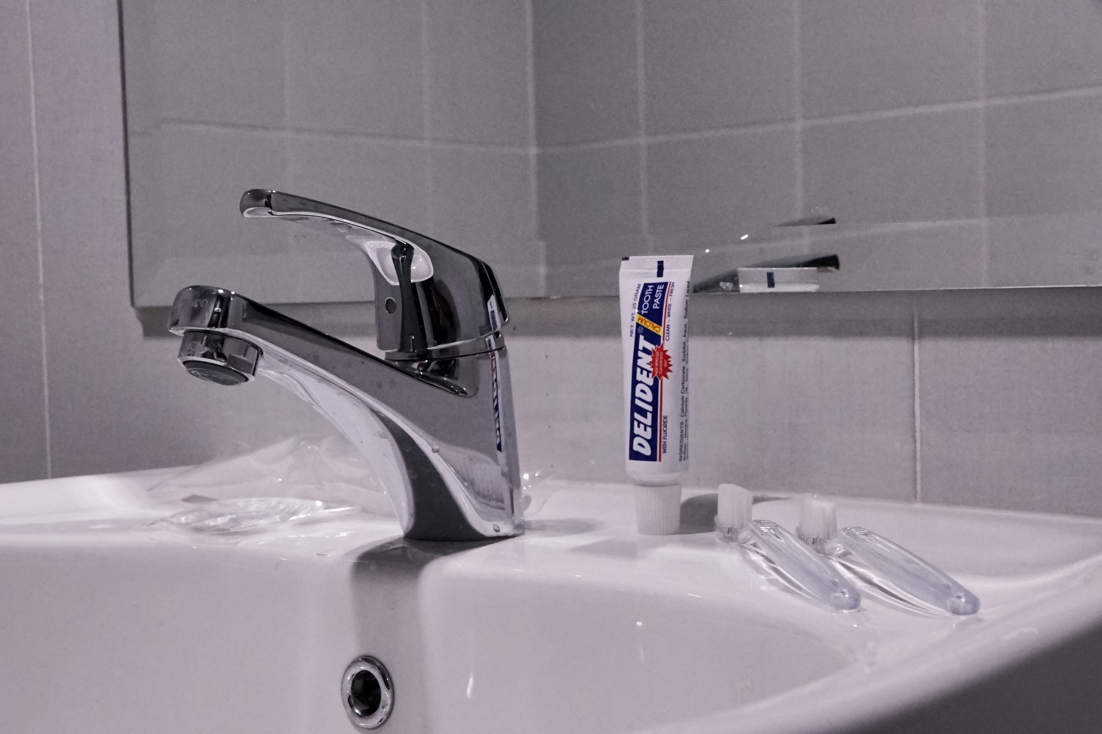 A bathroom sink with a modern faucet and a tube of Deliex toothpaste.