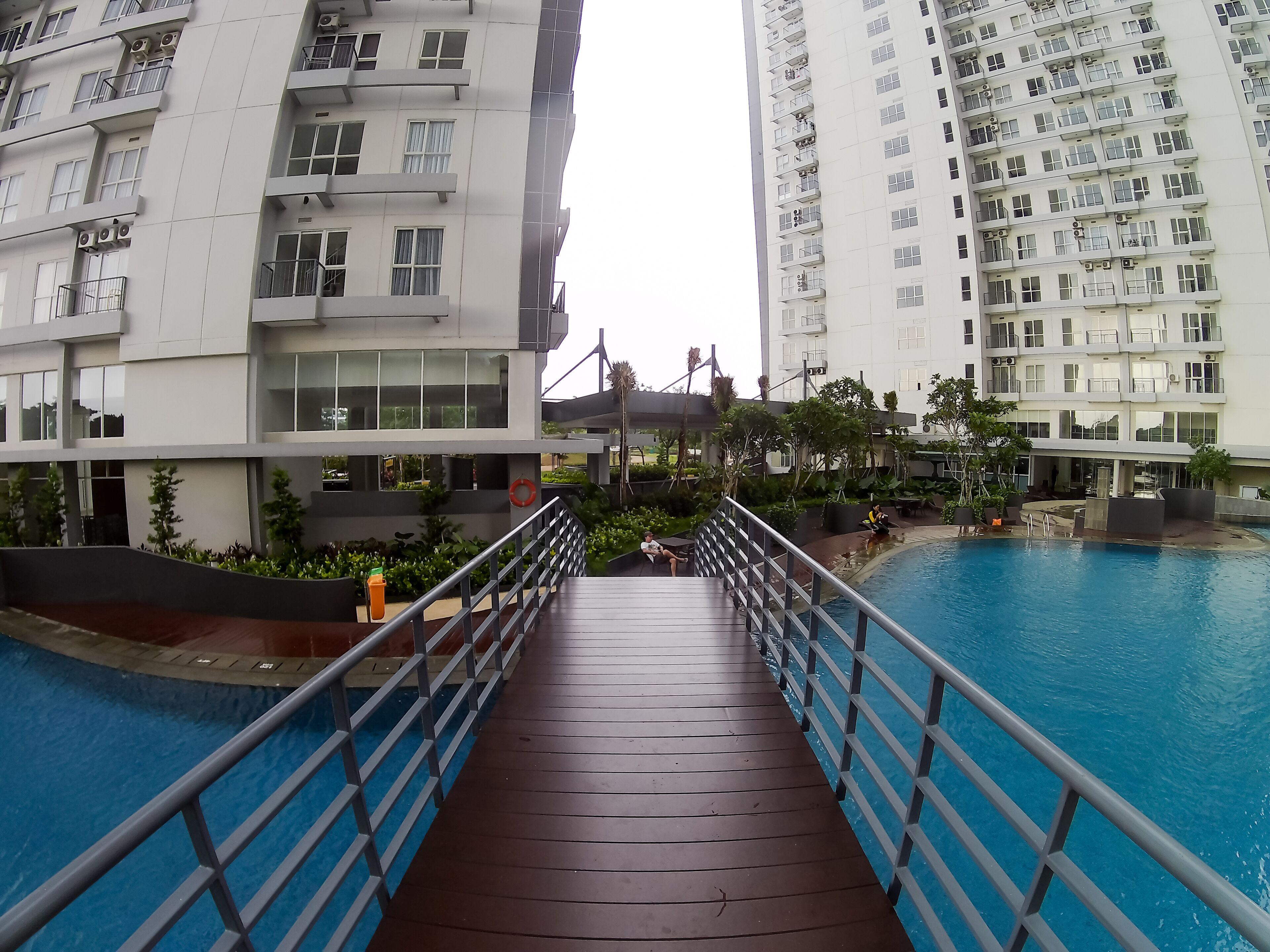 A modern hotel with a pool area, a wooden deck, and a view of adjacent high-rise buildings.