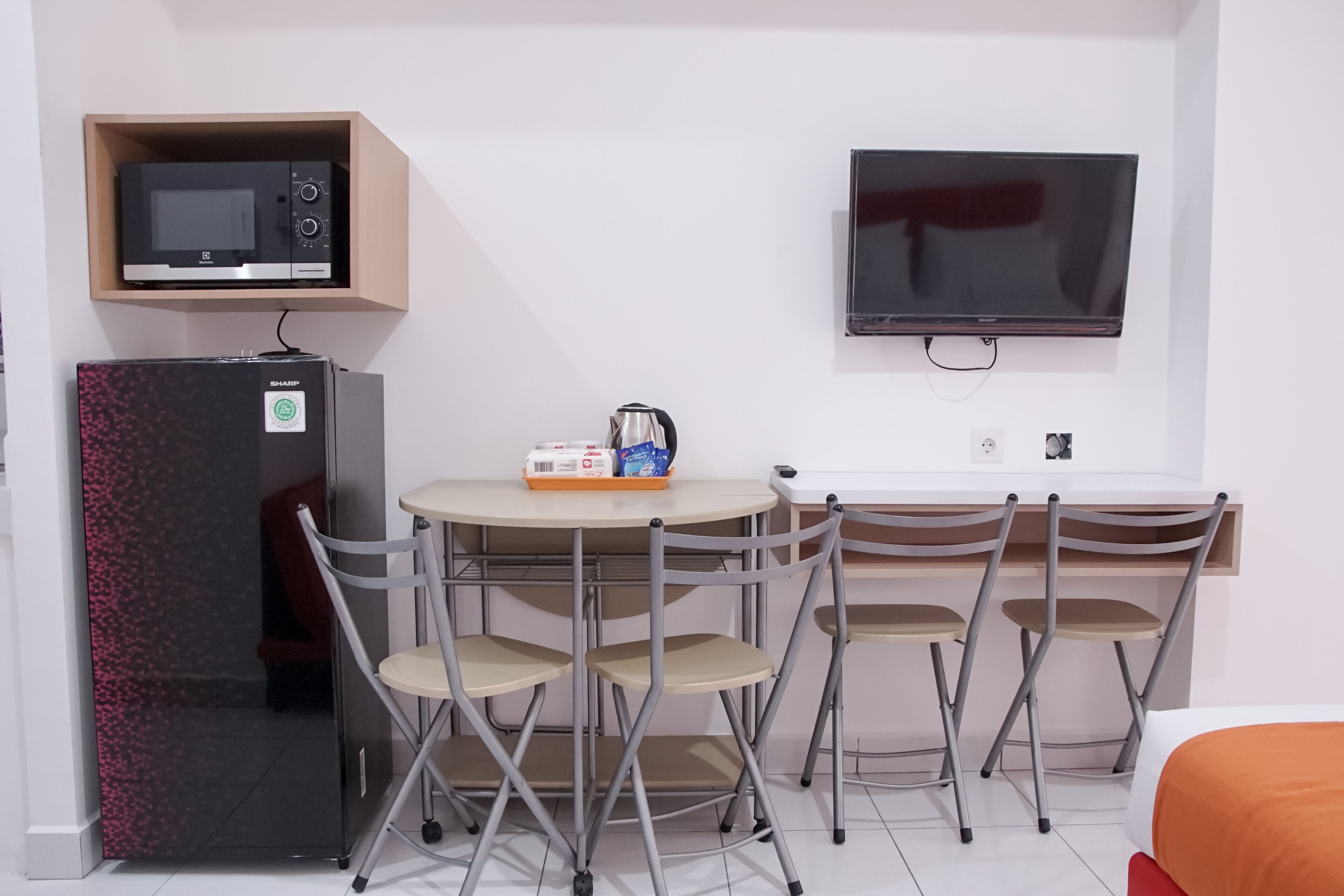 Habitación compacta con kitchenette, televisor de pantalla plana, mesa plegable y cuatro sillas.